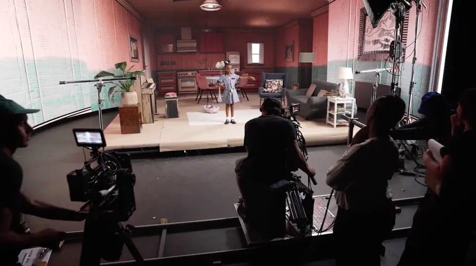 Behind the scenes on a video shoot: crew and cameras around a staged living-room set